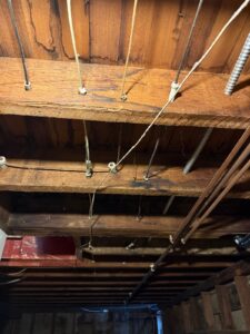 Knob-and-tube wiring suspended across exposed basement ceiling joists